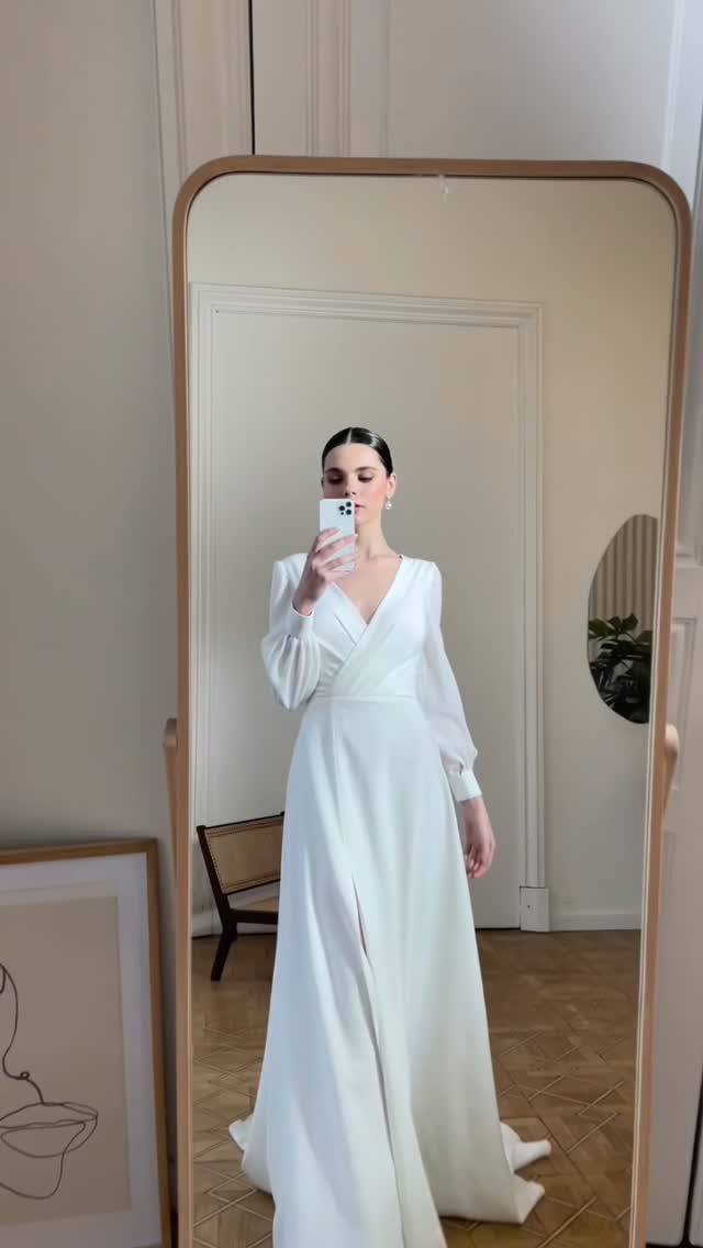 Woman in a minimalist long-sleeved white wrap dress posing for a mirror selfie.