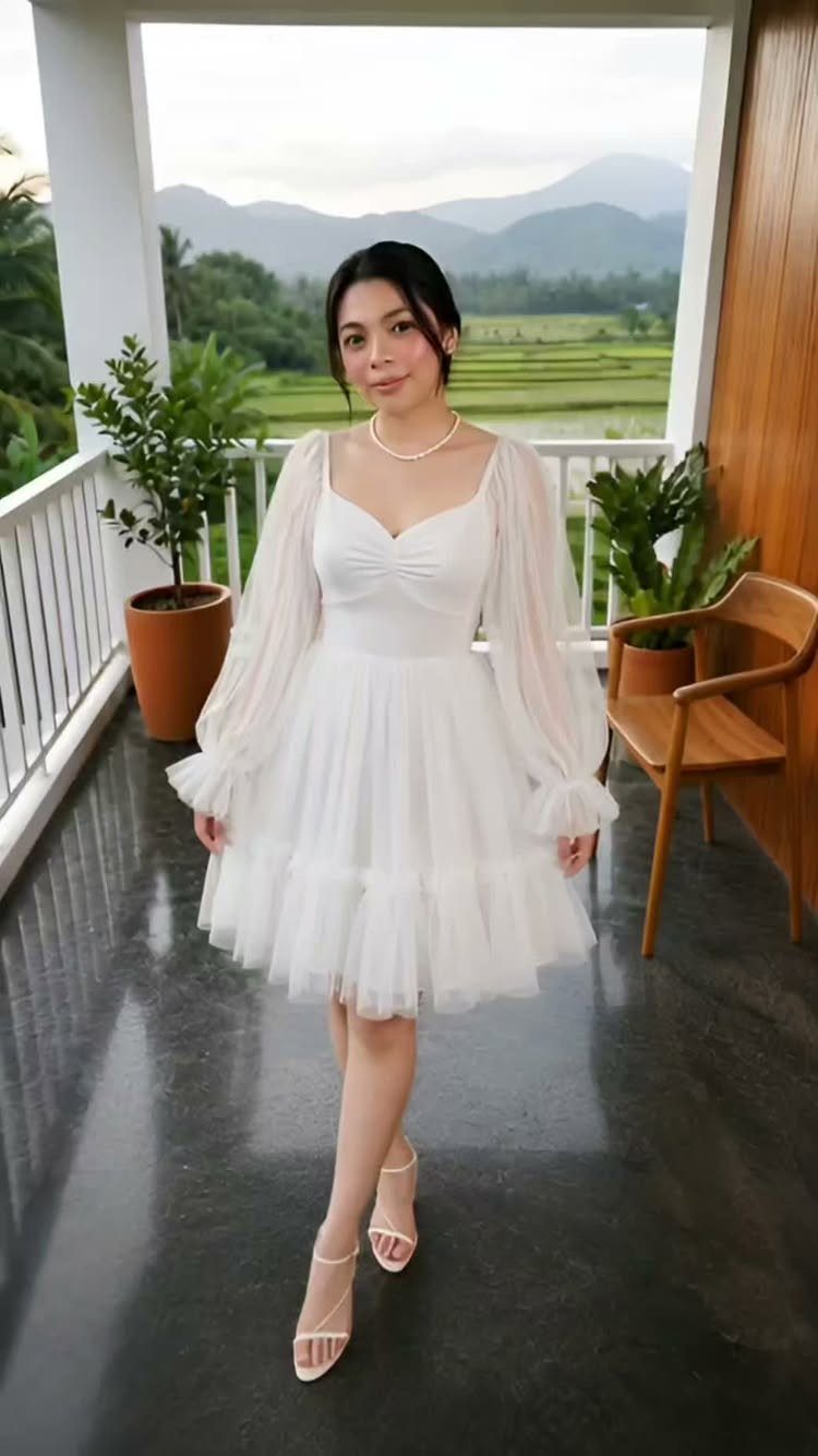 Woman in a short white tulle cocktail dress with puff sleeves on a balcony.