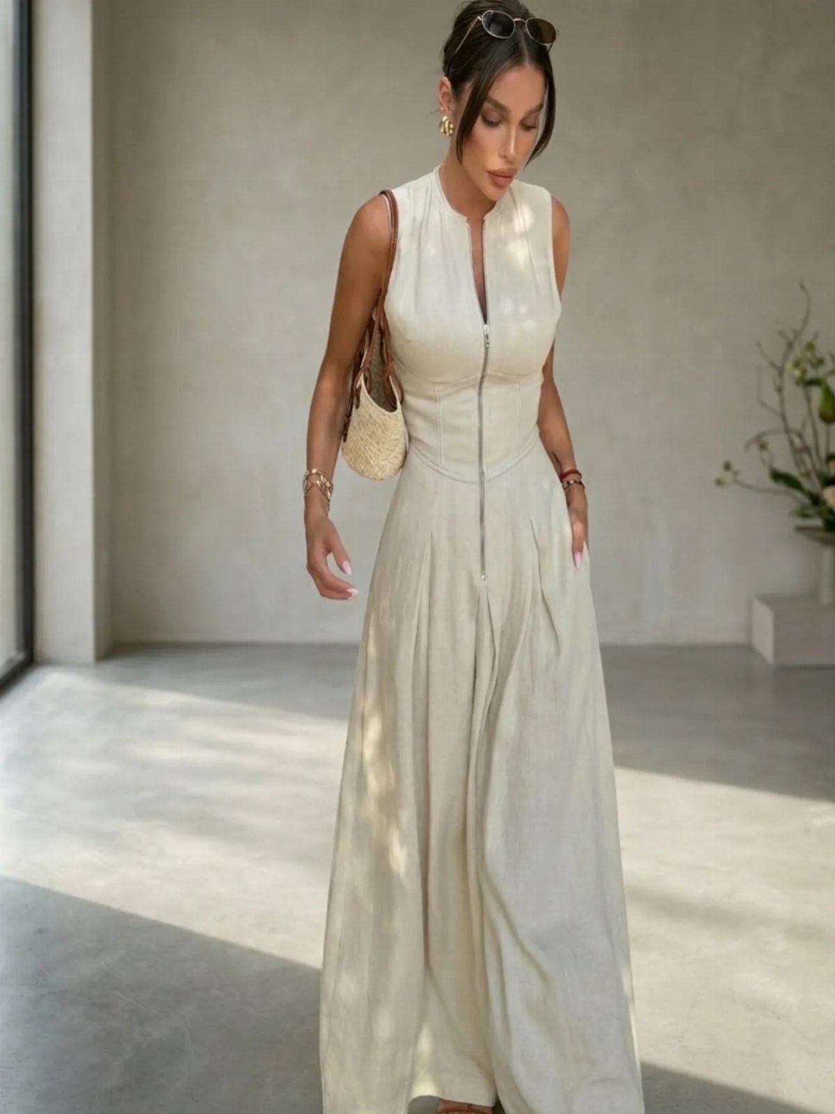 Woman in a sleeveless white maxi dress with a front zipper and woven bag.
