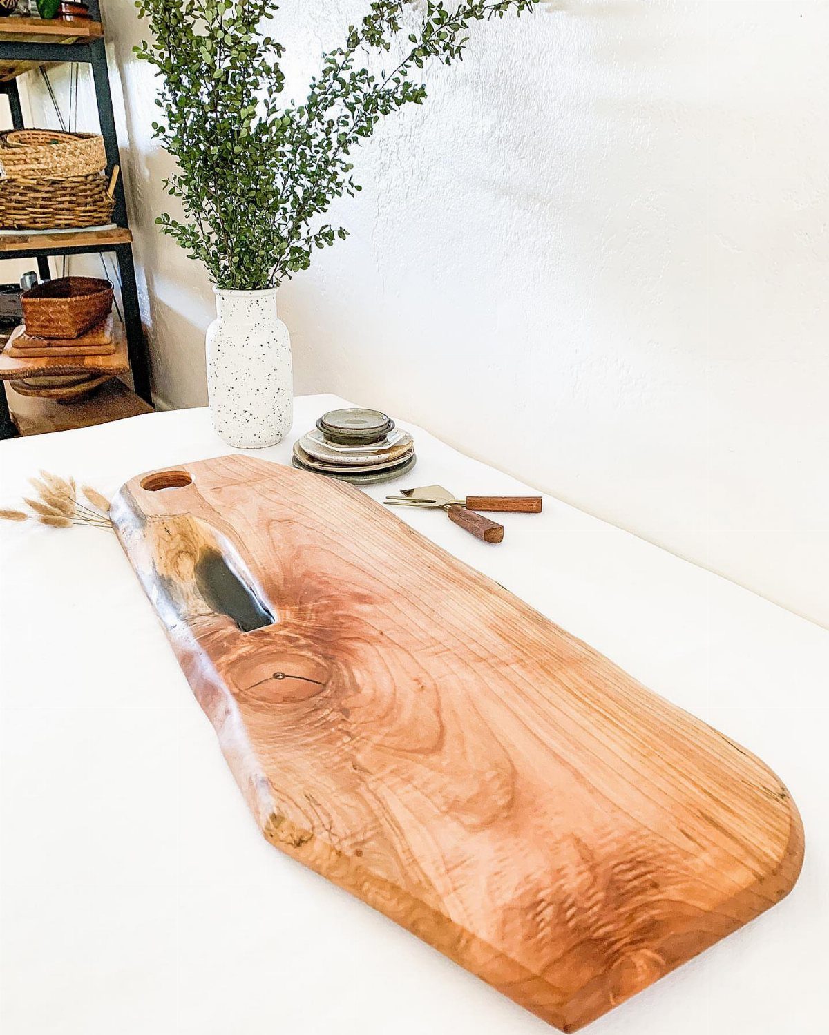 Live-edge wooden cheese board with resin fill on a white table with greenery