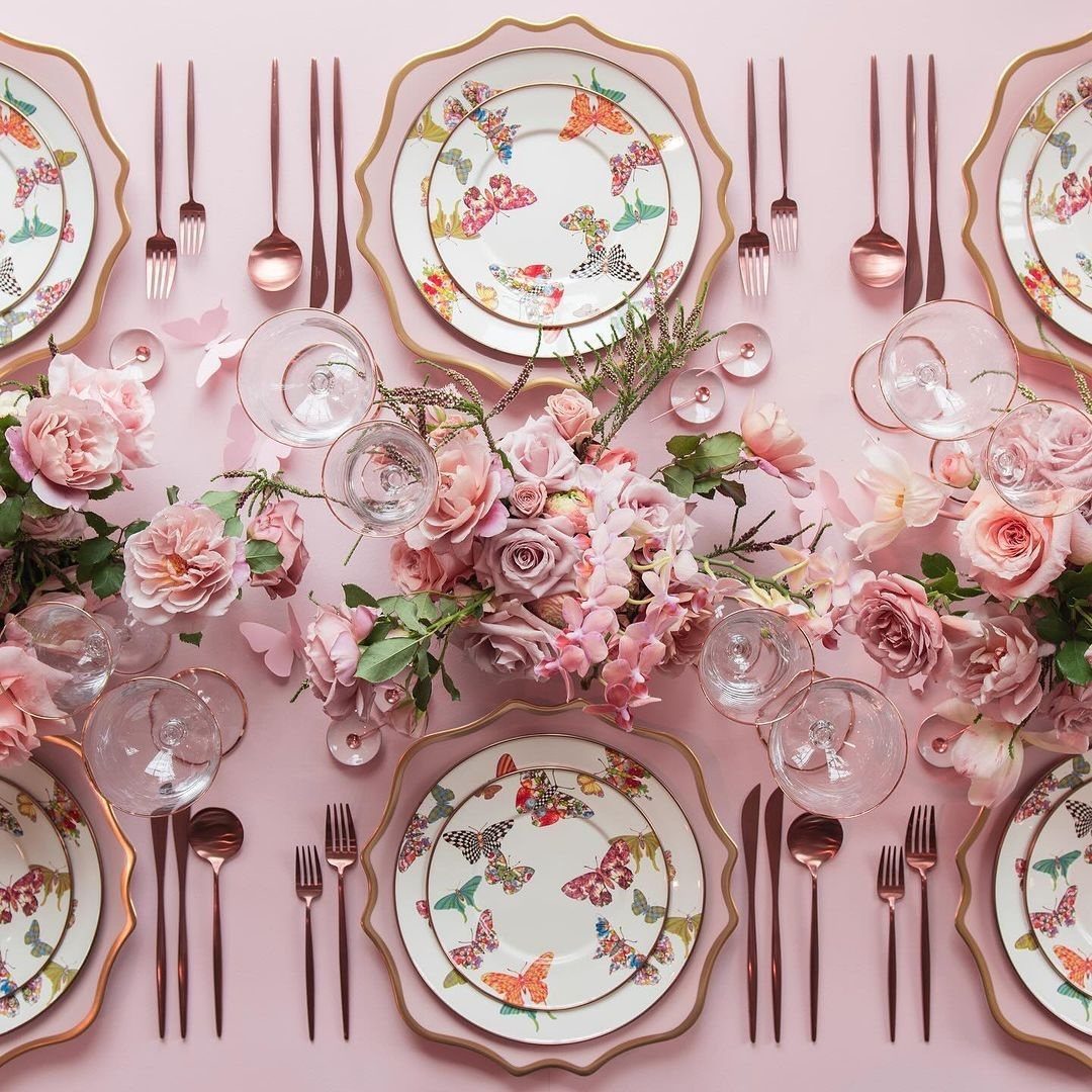 Butterfly patterned ceramic plates and rose-gold cutlery on a pink table with roses