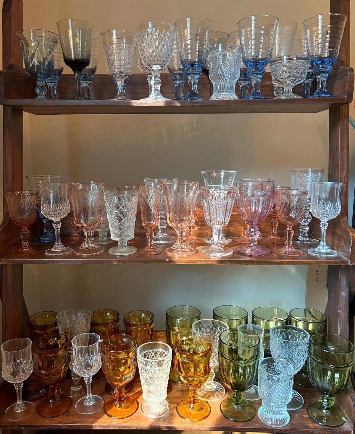 Vintage colorful glassware and goblets displayed on three rustic wooden shelves.
