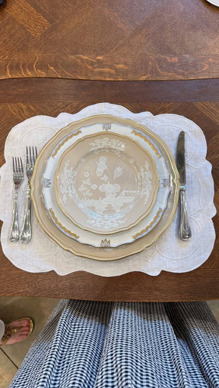 Elegant place setting with gold-rimmed plates and silver cutlery on a white placemat.