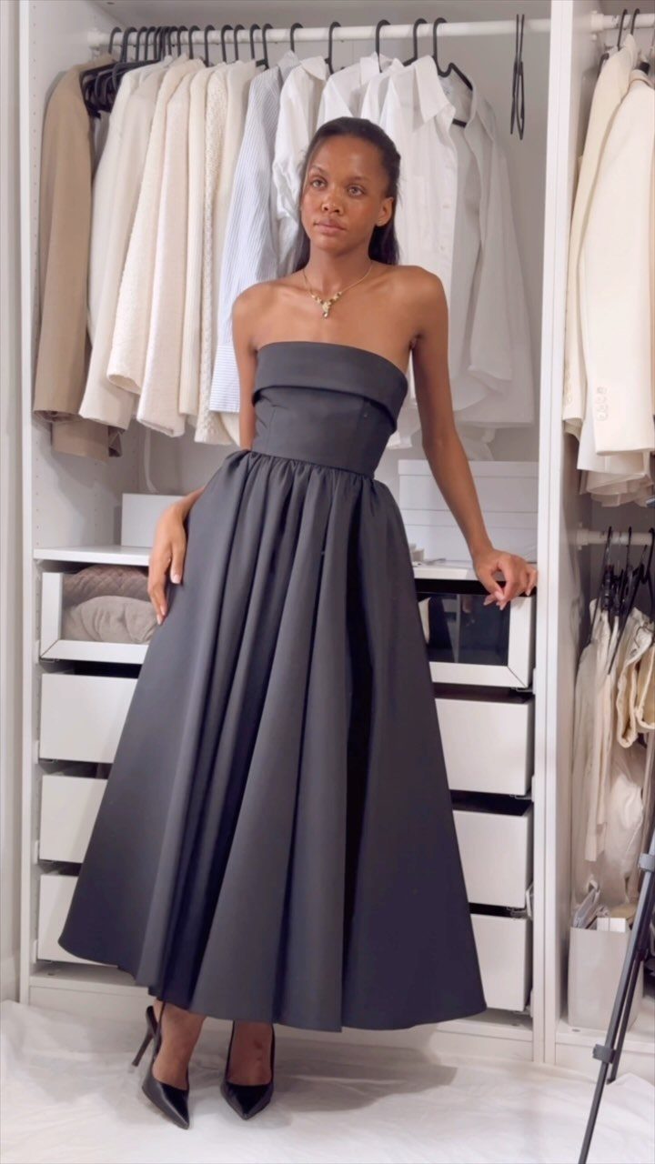 Woman in a strapless charcoal grey floor-length gown posing in a white closet.