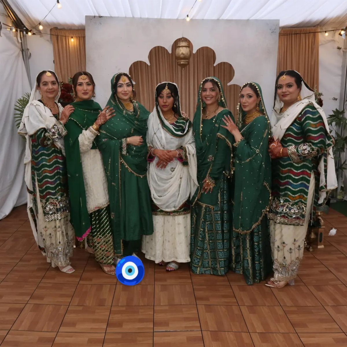 Seven women in traditional green and white South Asian wedding guest attire posing together.