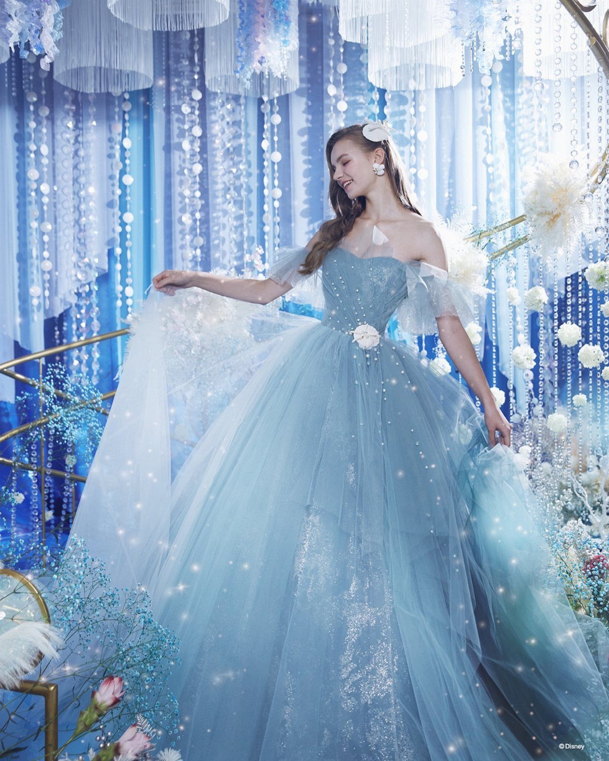 Woman in a sparkling light blue tulle ballgown posing against a blue backdrop.