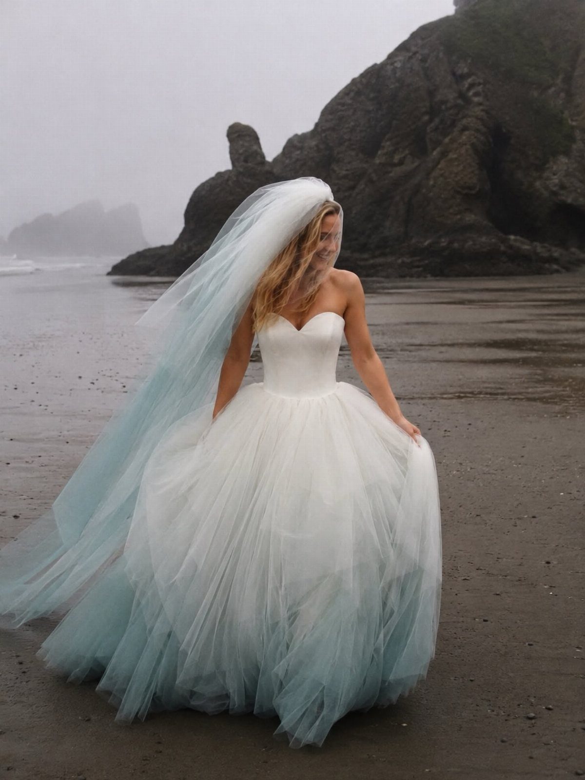 Woman in white wedding gown with teal ombre skirt and veil on beach