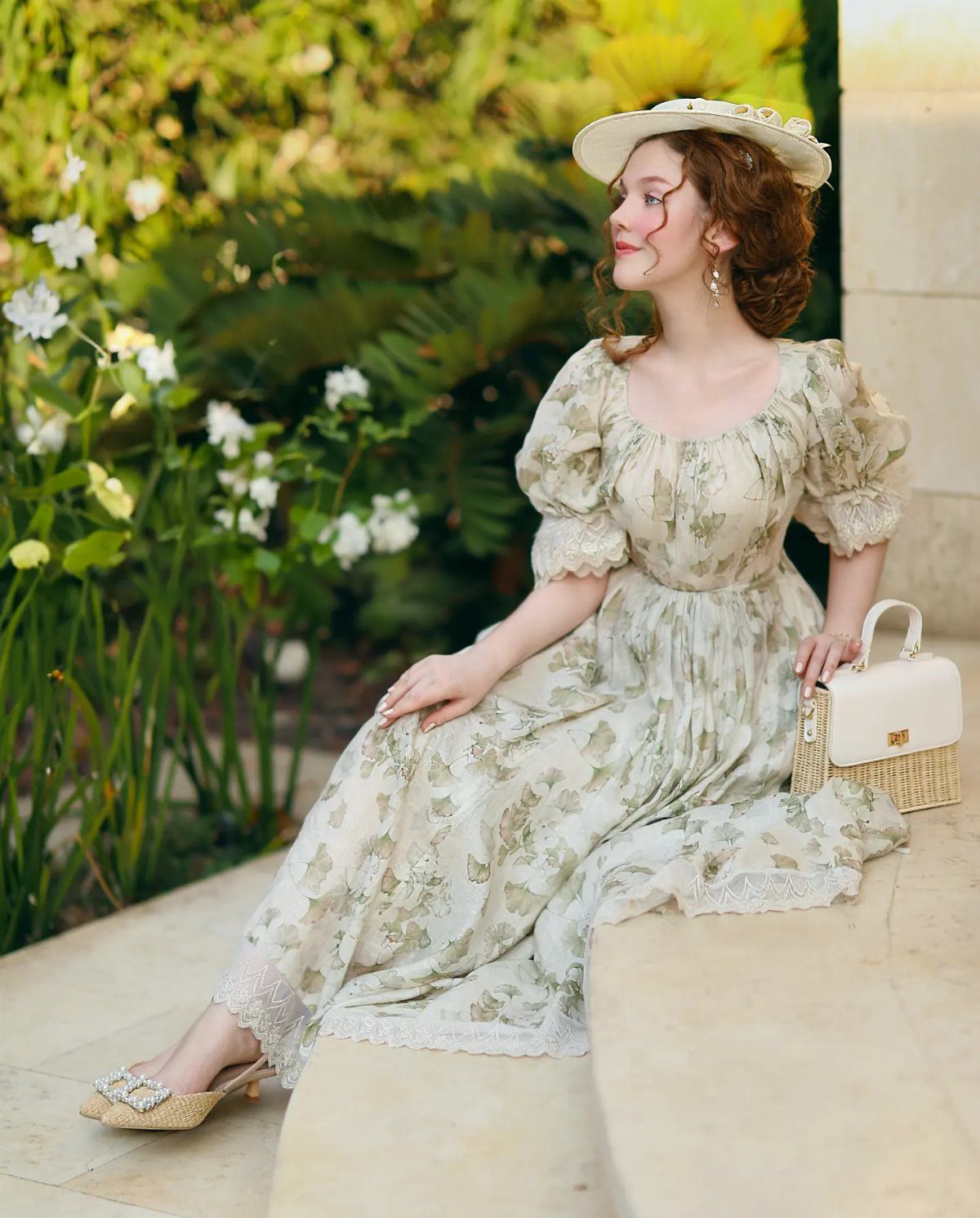 Woman in floral dress and straw hat sitting in a garden with a handbag.