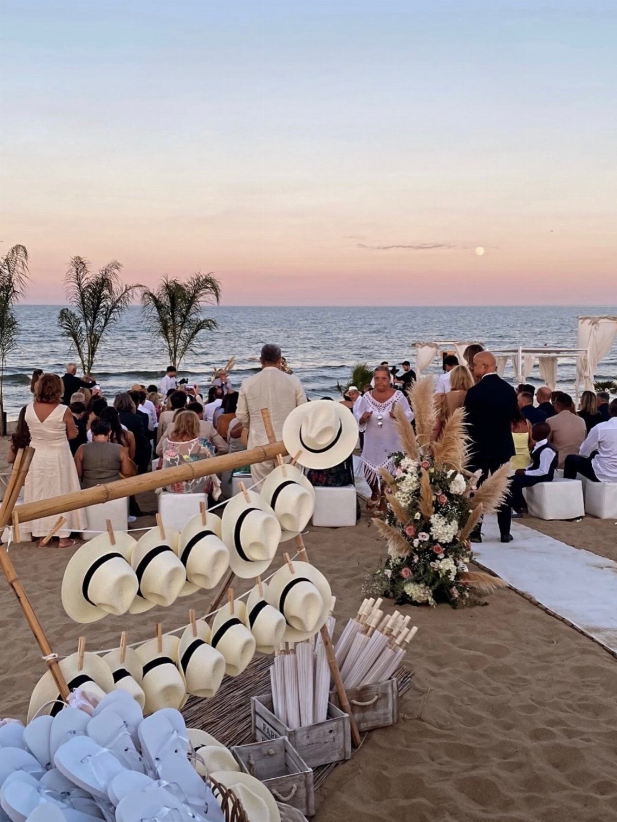 White sun hats on a wooden display rack at a beach wedding ceremony