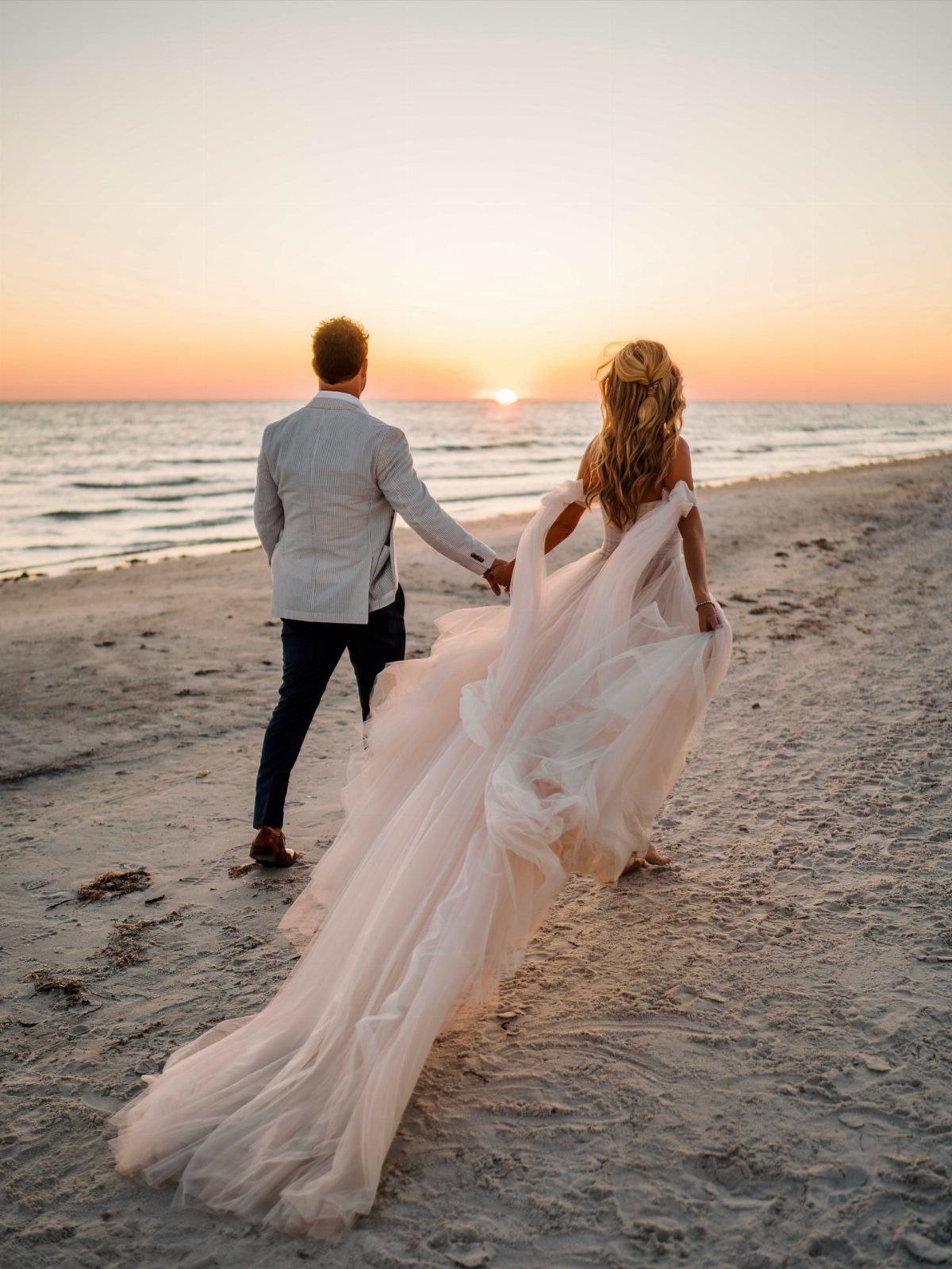 Bride in a voluminous pink A-line wedding gown walking on a beach at sunset