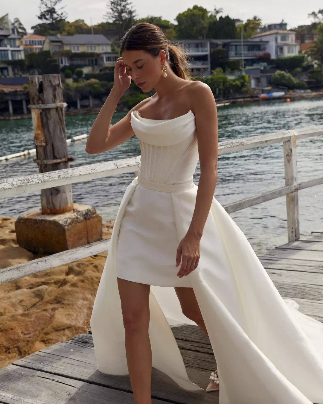 Woman in a white strapless mini wedding dress with a long overskirt on a pier.