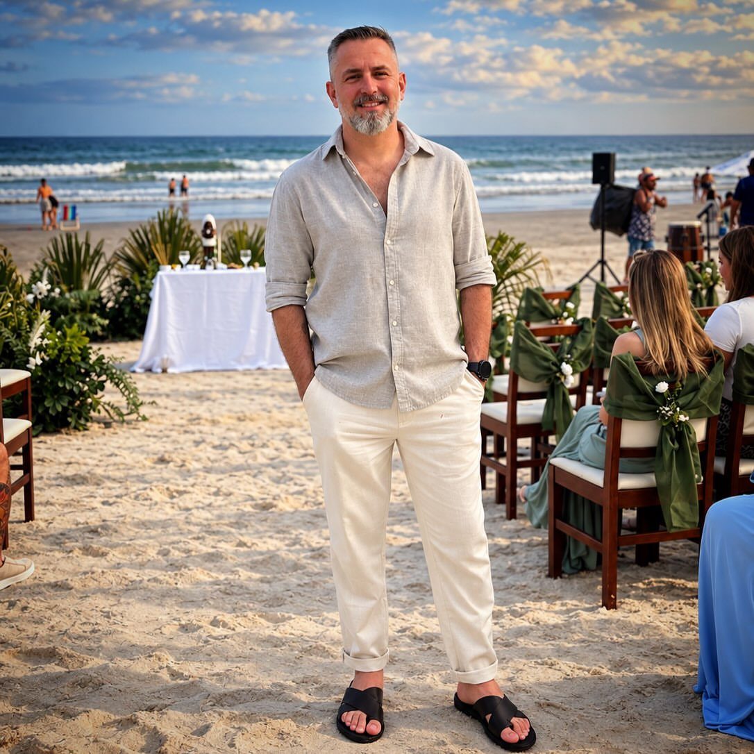 Man wearing a grey linen shirt and white trousers at a beach wedding.
