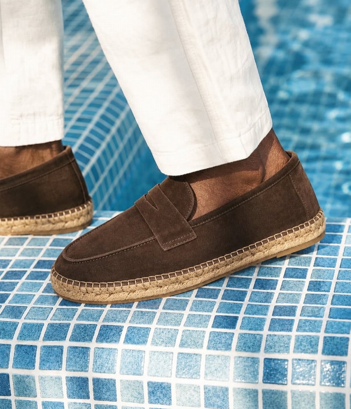 Brown suede espadrilles with jute soles and white trousers on blue tiled steps.