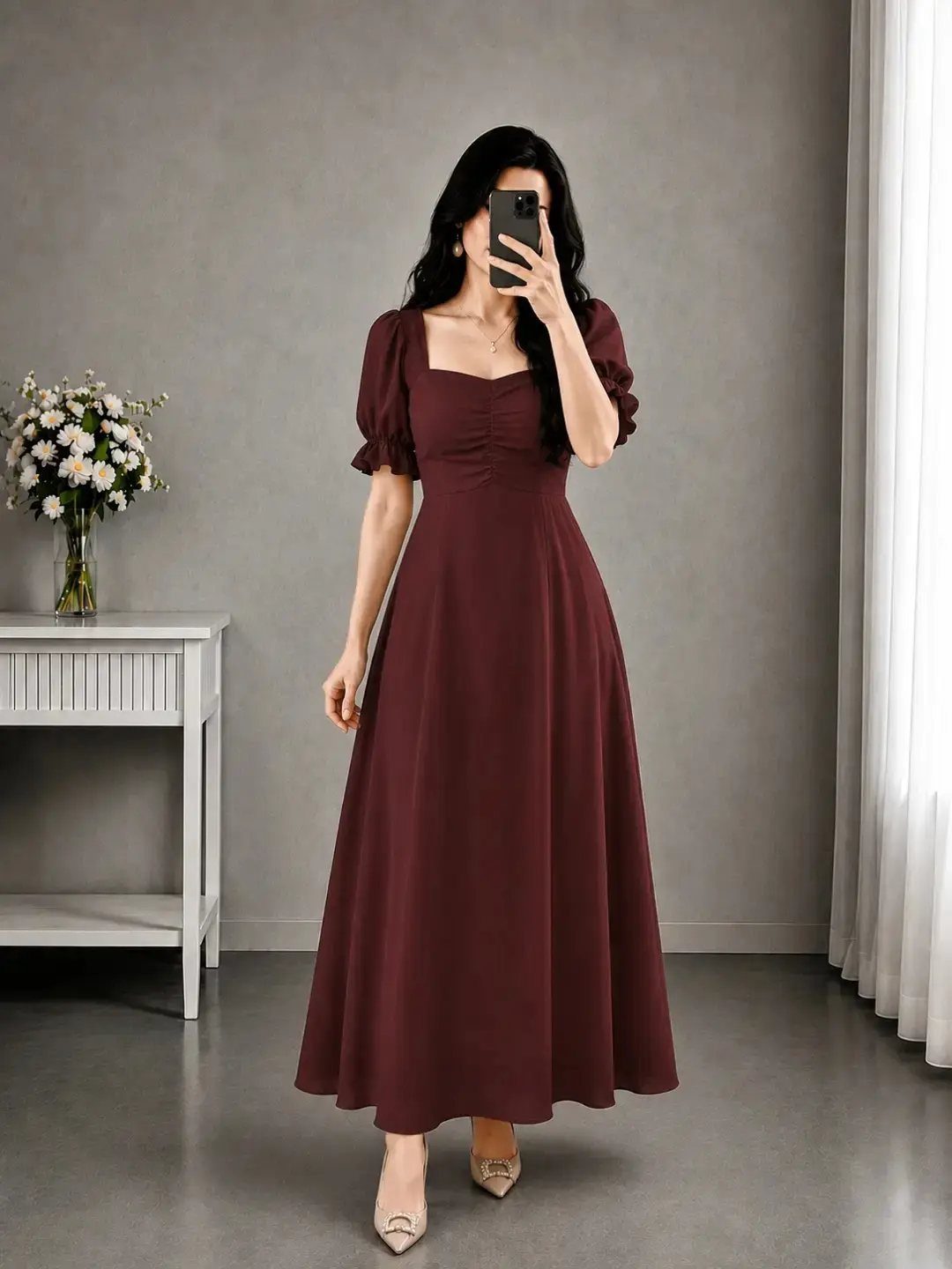 Woman wearing a burgundy maxi dress with puffed sleeves in a grey room.