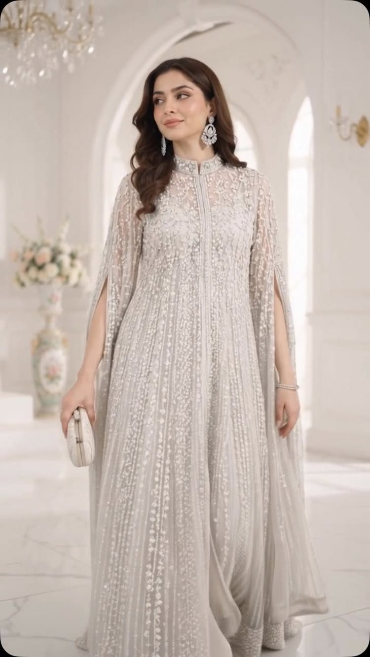 Woman in a silver-grey embellished maxi dress with cape sleeves in a bright room.