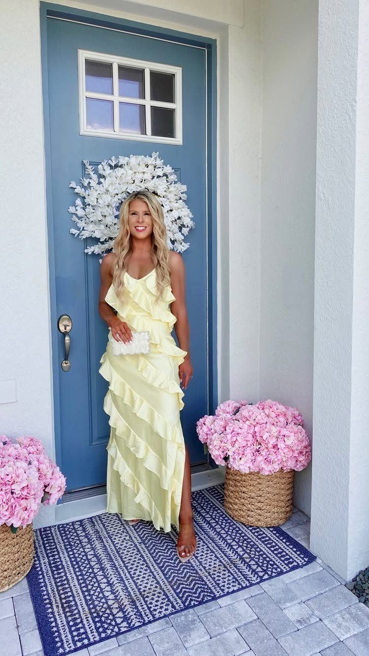 Woman in a pale yellow ruffled maxi dress standing before a blue door.