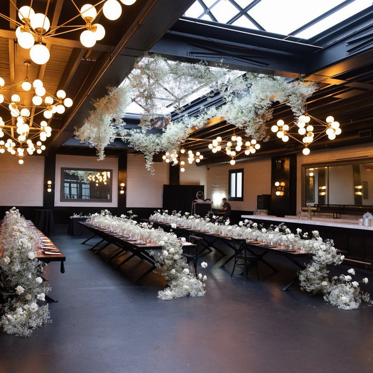 Industrial wedding venue with long tables, white floral arrangements, and modern globe lighting.