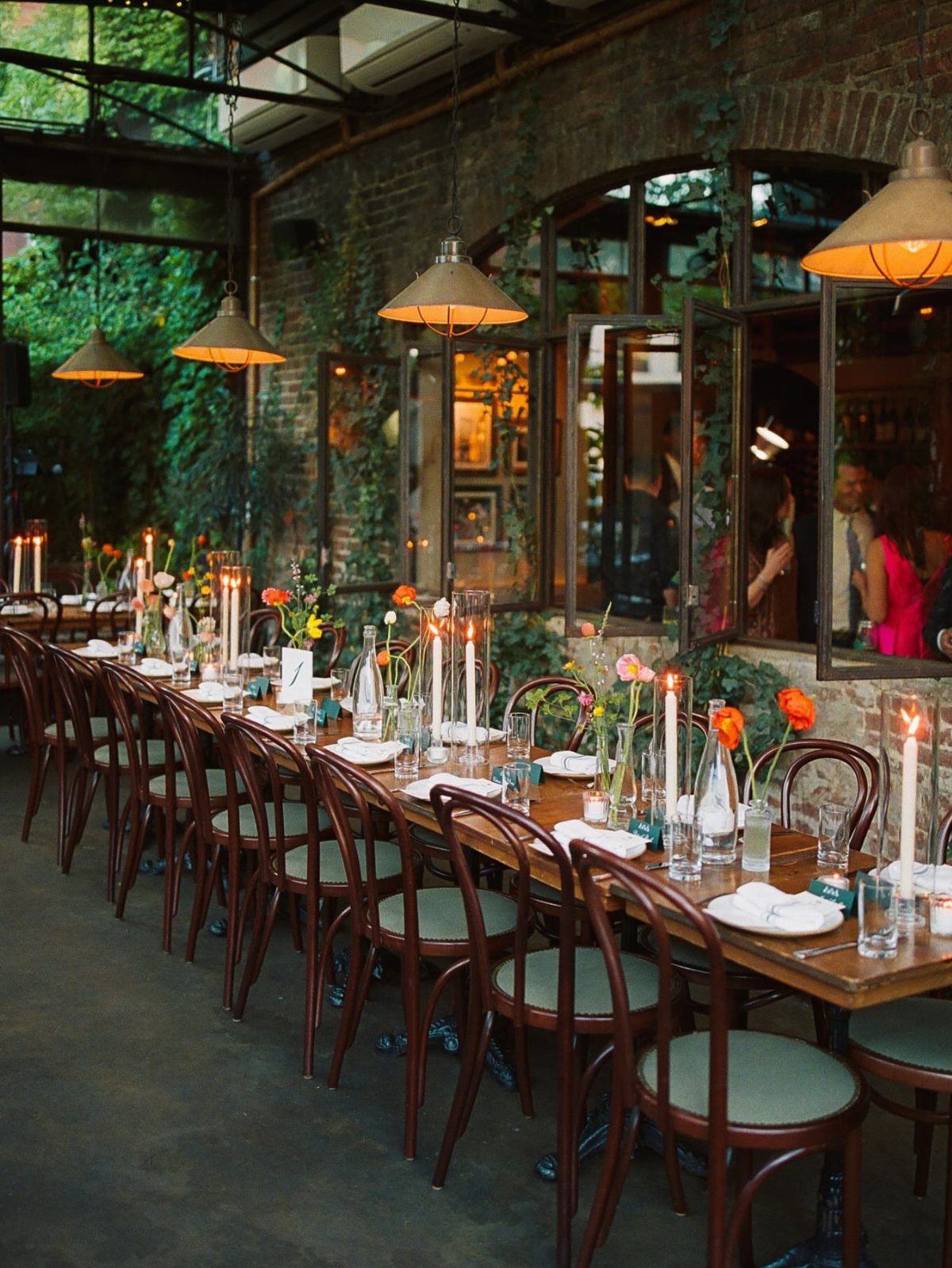 Long wooden dining table with candles and bentwood chairs in an outdoor patio.