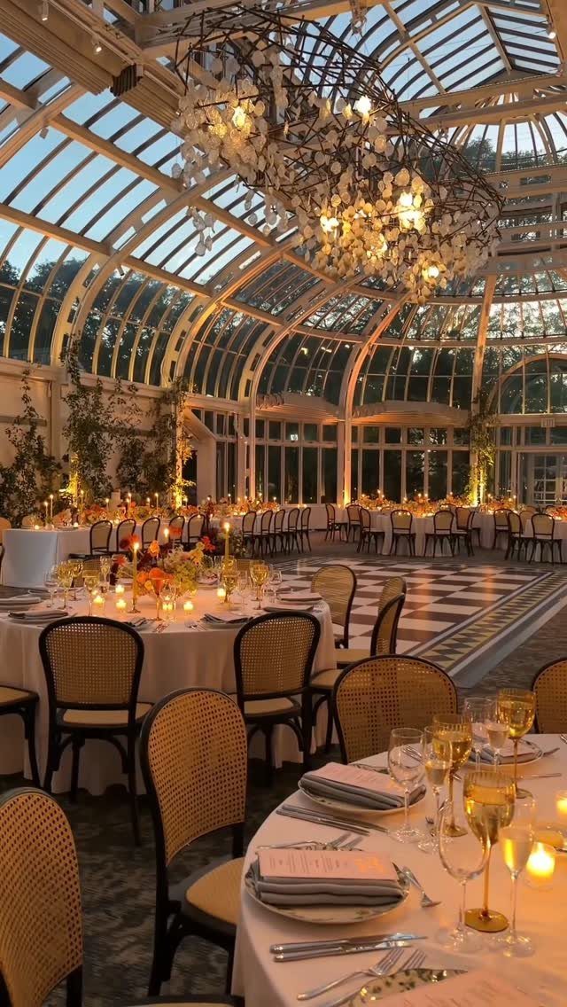 Wedding reception tables and a dance floor inside a glass conservatory with a chandelier.
