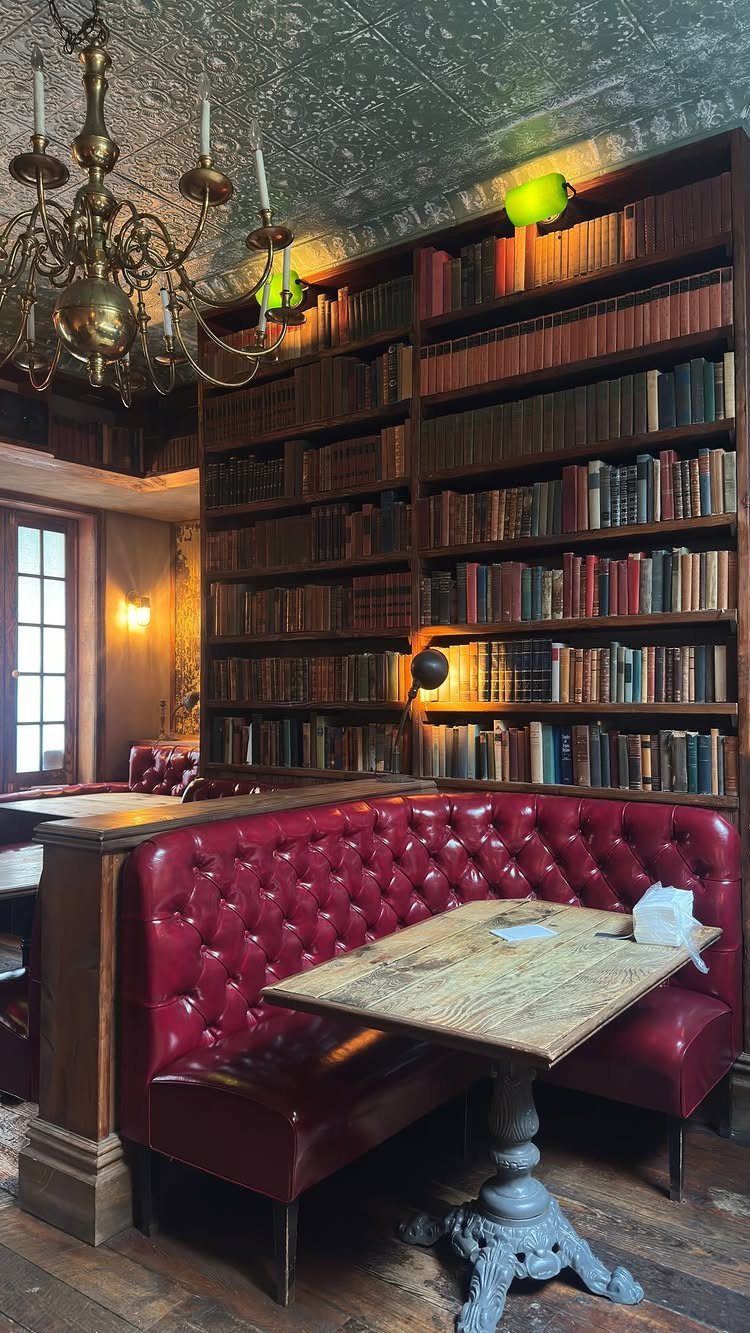 Red tufted leather booth and wooden table next to large bookshelves in a restaurant.