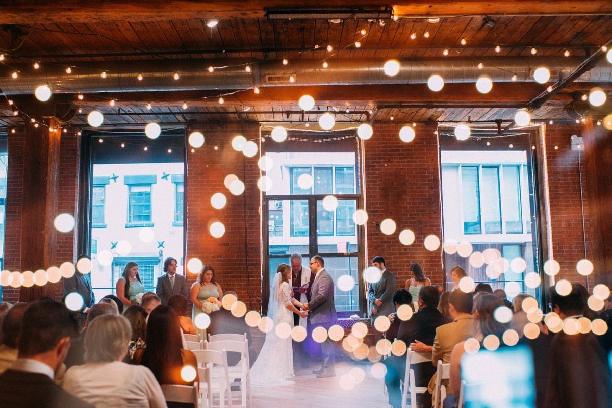 Wedding ceremony in an industrial loft with brick walls and glowing fairy lights.