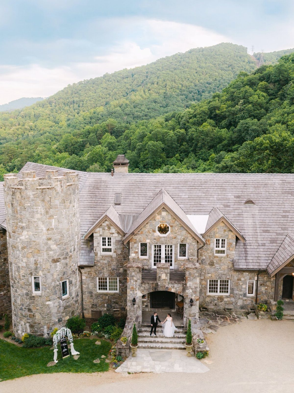 Stone castle with a bride and groom at the entrance against green mountains.