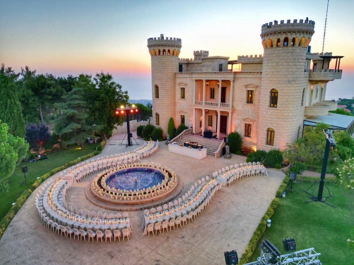 Large stone castle with white wedding chairs arranged around a circular blue fountain.