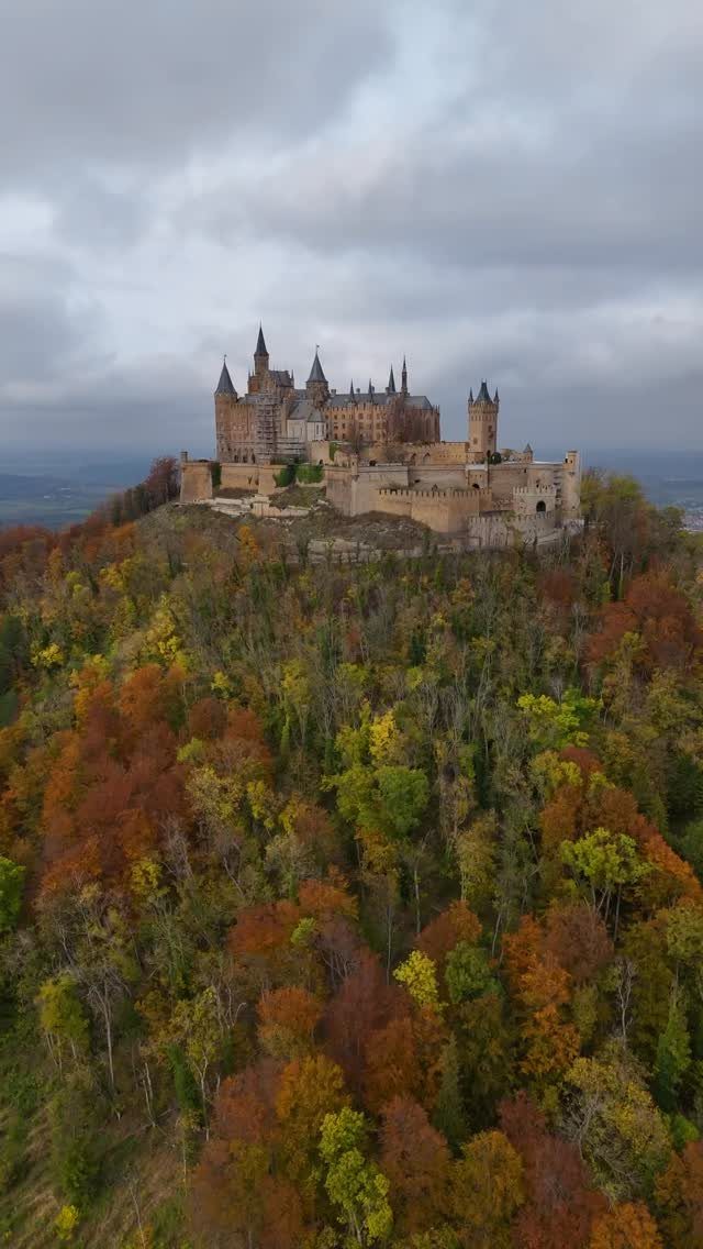 Stone castle with many turrets atop a hill surrounded by colorful autumn forests.