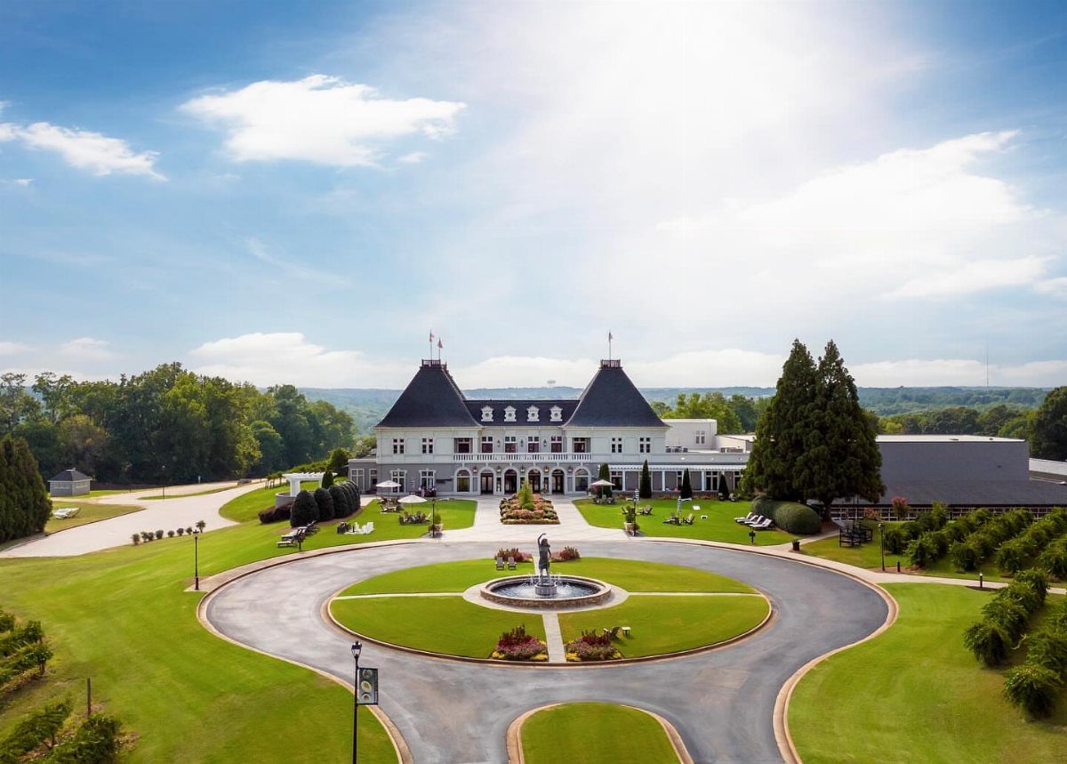 Large white luxury estate with black towers and a circular fountain driveway.