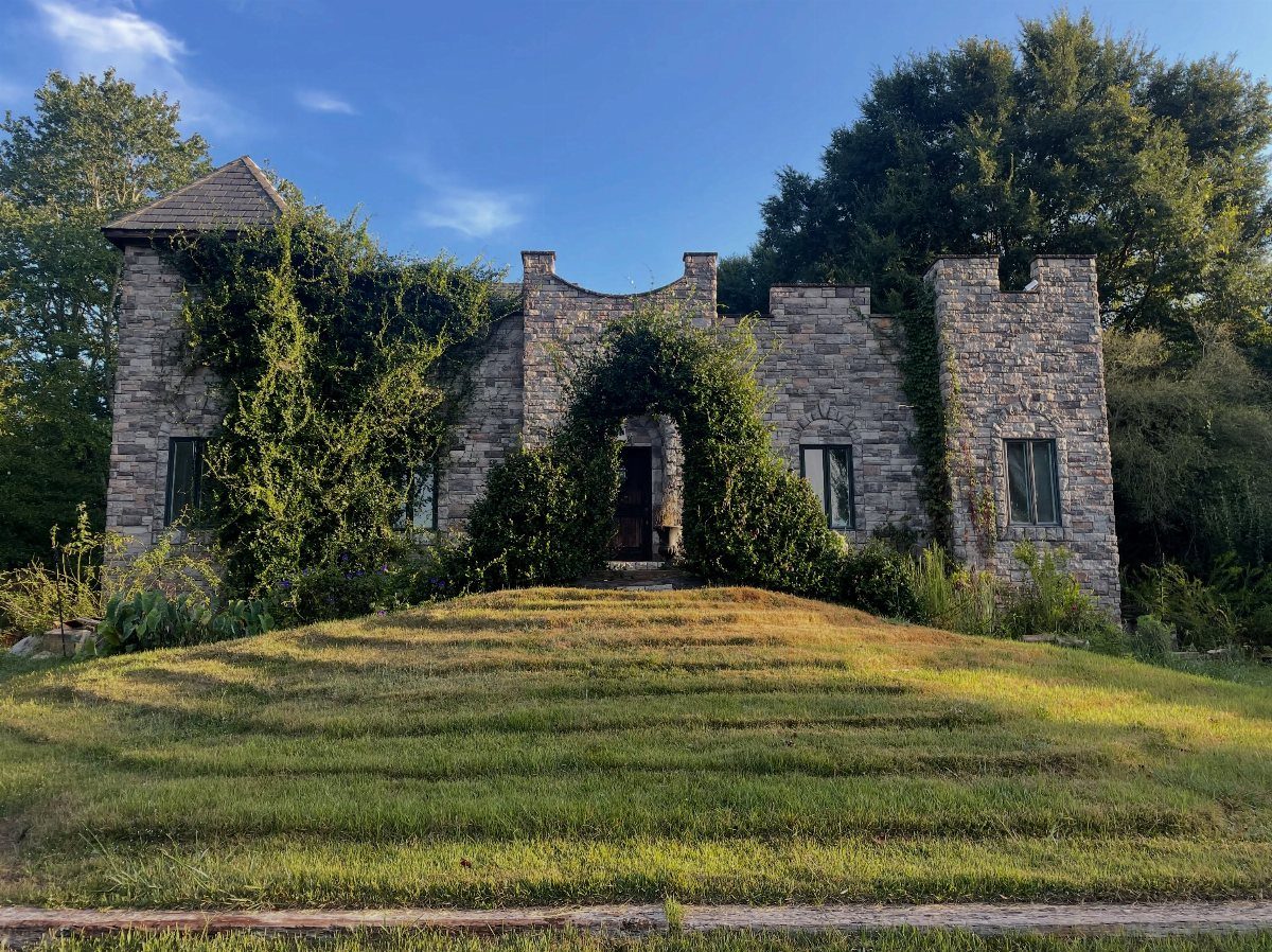 Grey stone castle with climbing vines on a grassy hill under blue sky
