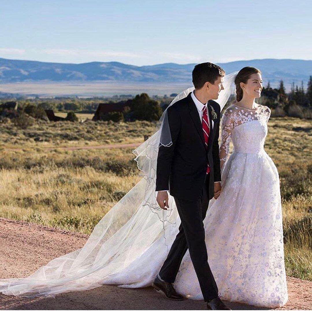 Bride in long-sleeved lace wedding dress walking with groom in a mountain landscape.