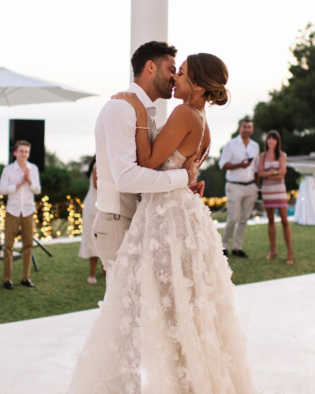Bride in floral wedding gown and groom kissing at an outdoor wedding ceremony.