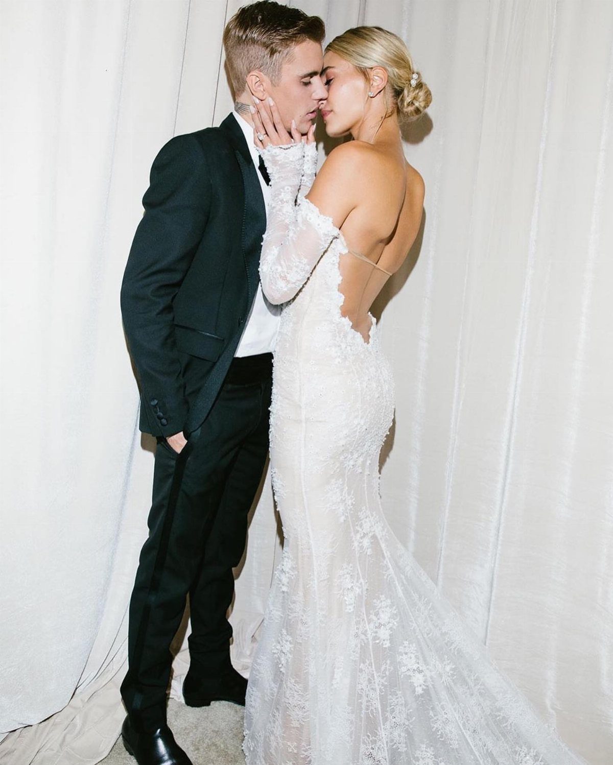 Bride in a white lace wedding gown and groom in a black suit kissing.