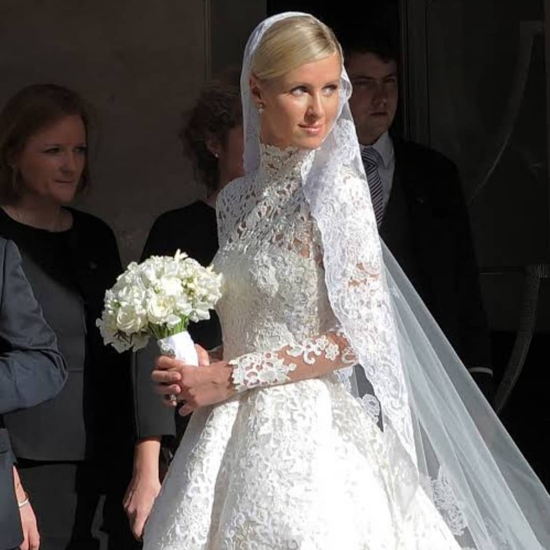 Woman in a high-neck white lace wedding gown holding a white flower bouquet.