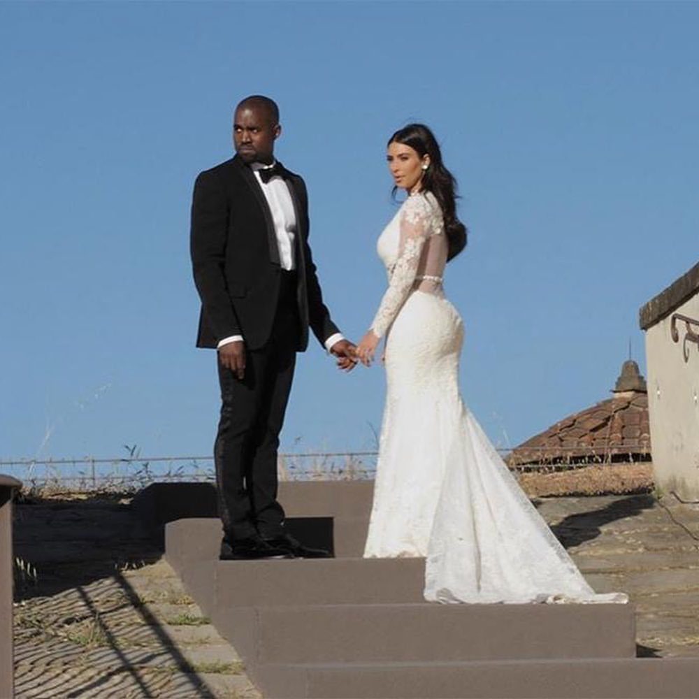 Kim Kardashian and Kanye West posing in their wedding attire on stone steps.