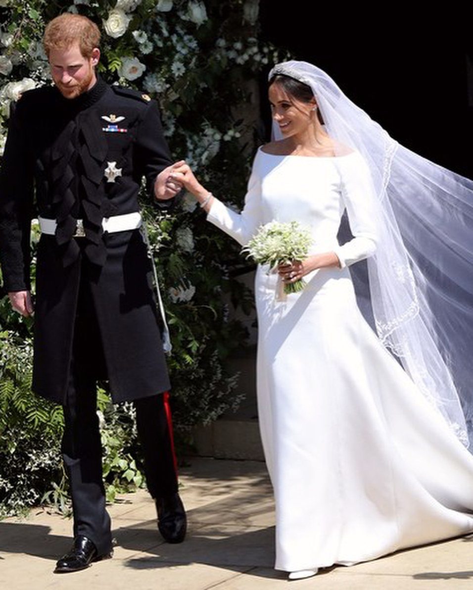 Meghan Markle in a minimalist white wedding gown and veil walking with Prince Harry.
