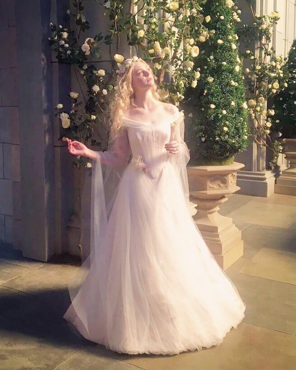 Woman in a white tulle wedding gown and floral crown in a rose garden.