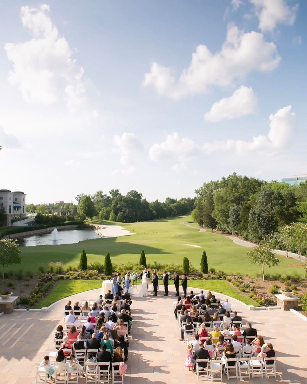 Outdoor wedding ceremony on a patio overlooking a scenic golf course and pond.