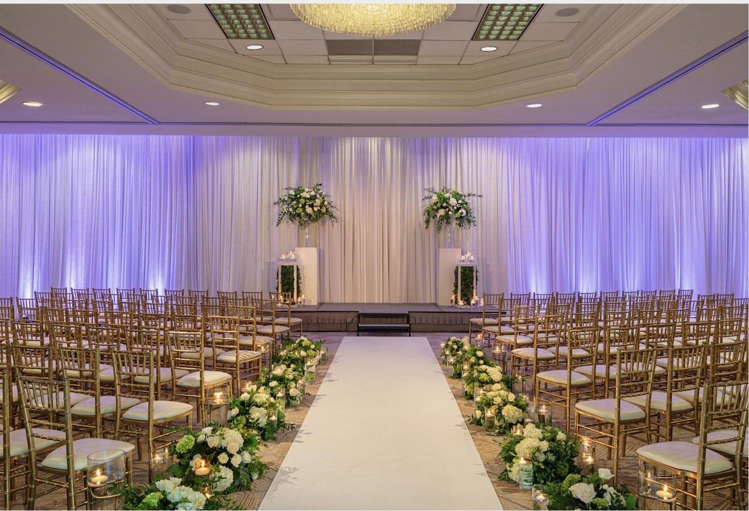 Wedding ceremony setup with gold chairs, white aisle, and purple lit drapery.