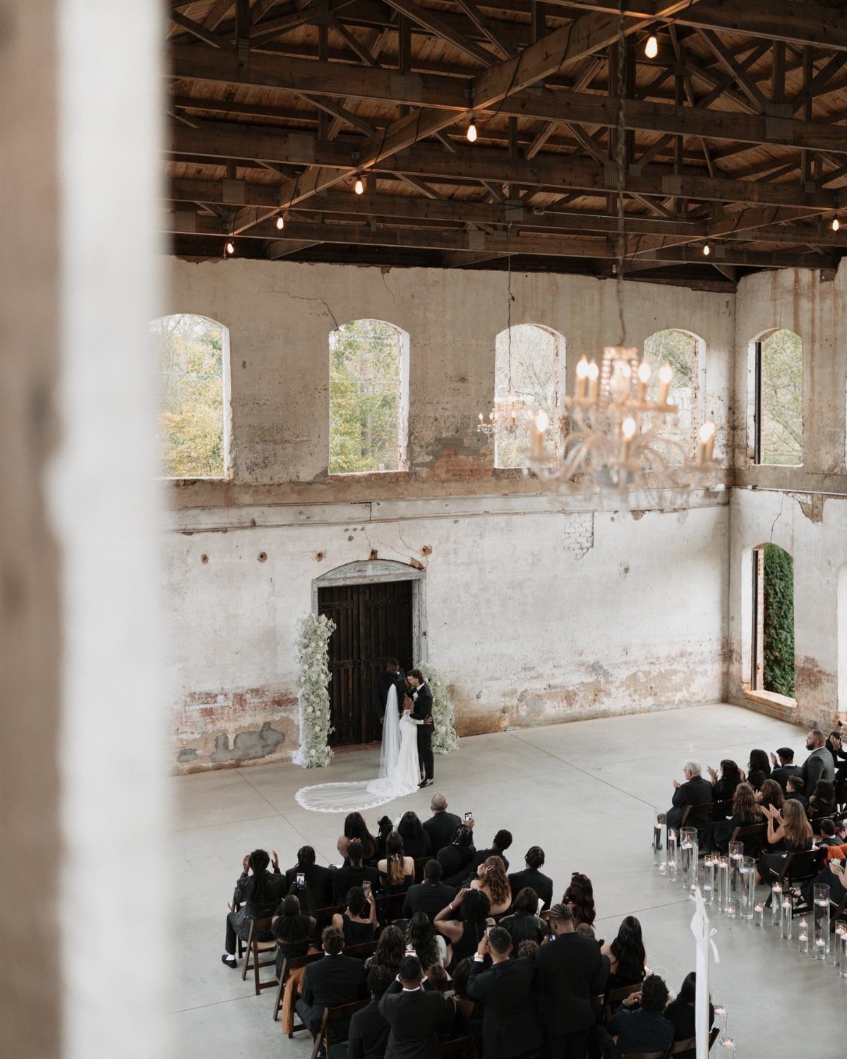 Wedding ceremony in a rustic industrial mill with white walls and wooden beams.