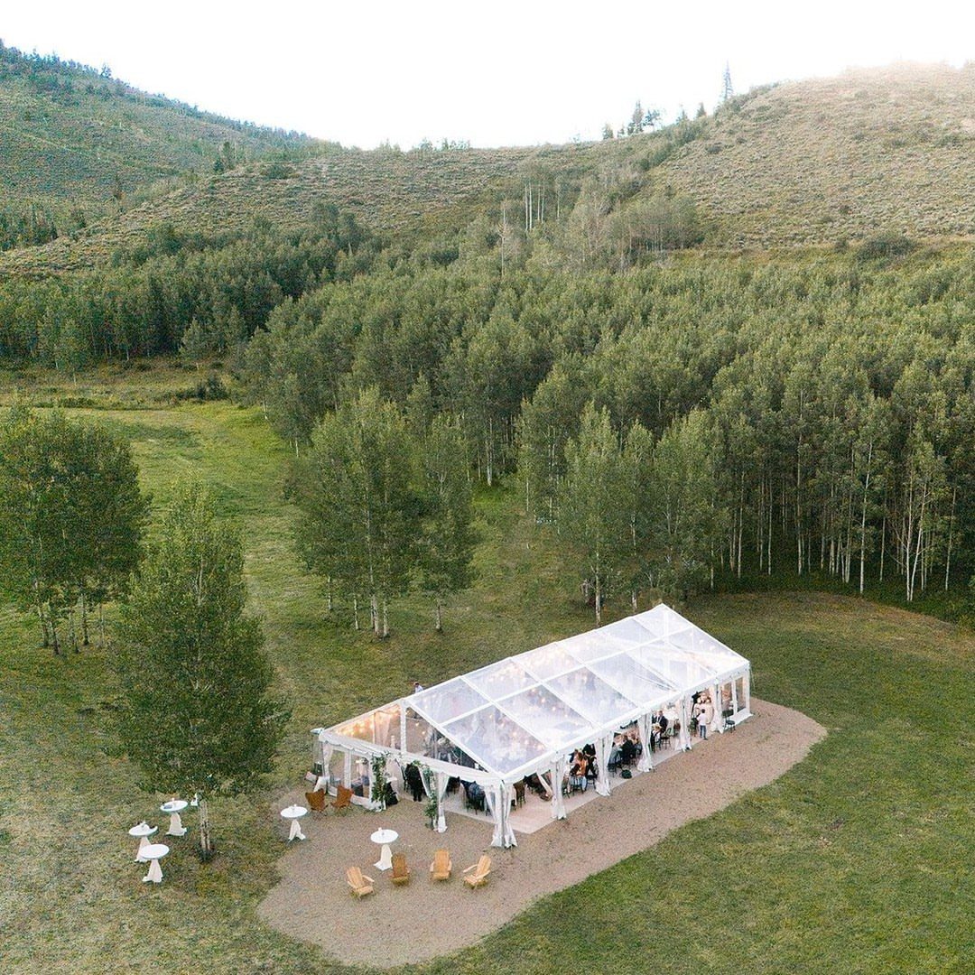Clear-top wedding tent in a mountain meadow surrounded by green aspen trees.