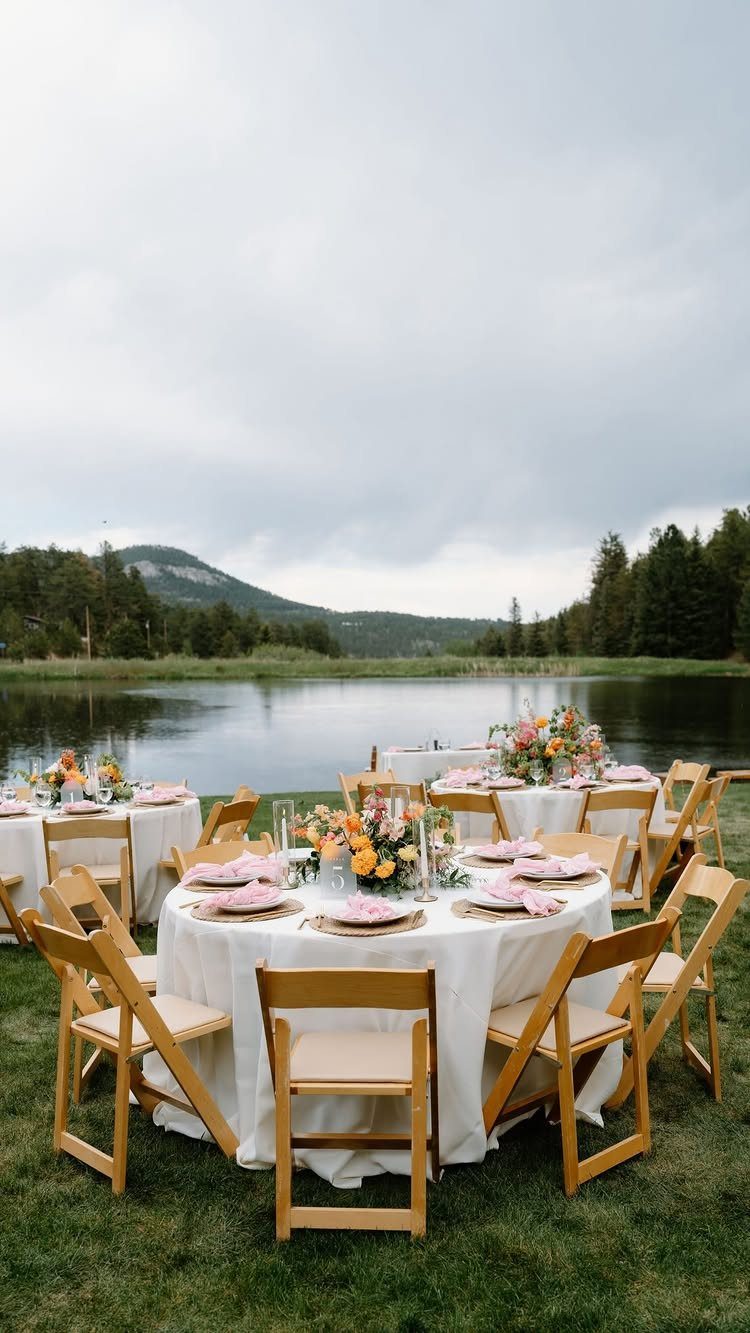 Outdoor wedding reception tables by a lake with mountains in the background