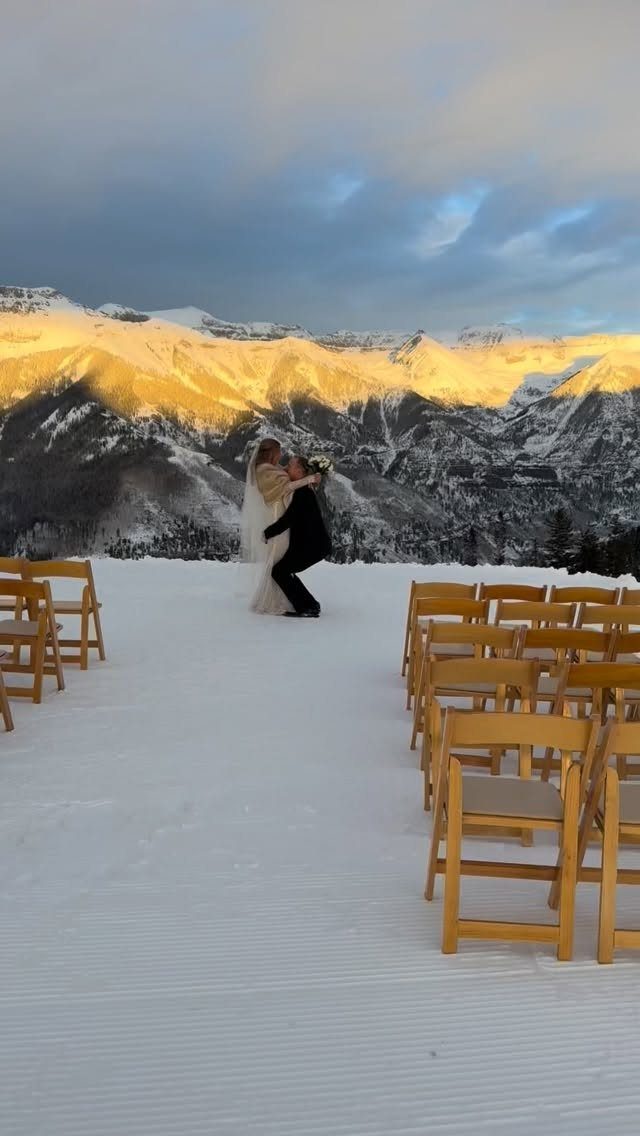 Bride and groom kissing at a snowy mountain wedding venue with wooden chairs.