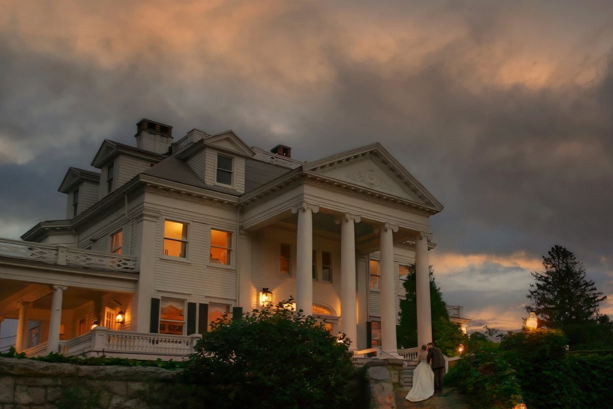 Historic white mansion with columns and a wedding couple at sunset
