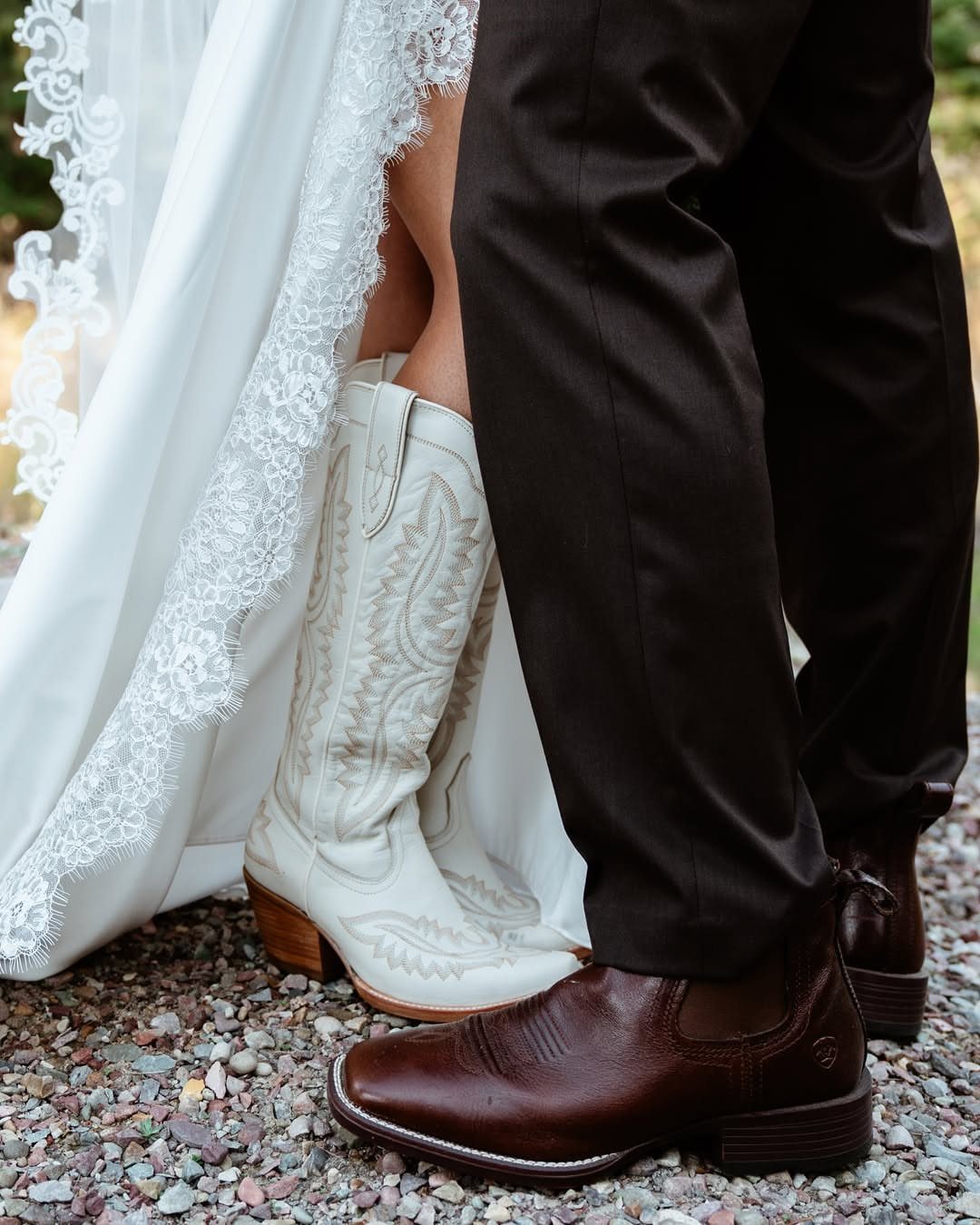White embroidered cowboy boots and brown leather boots on a gravel path.