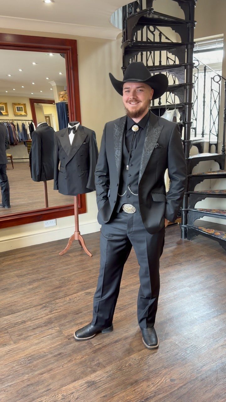 Man in a black western suit and cowboy hat posing in a store.