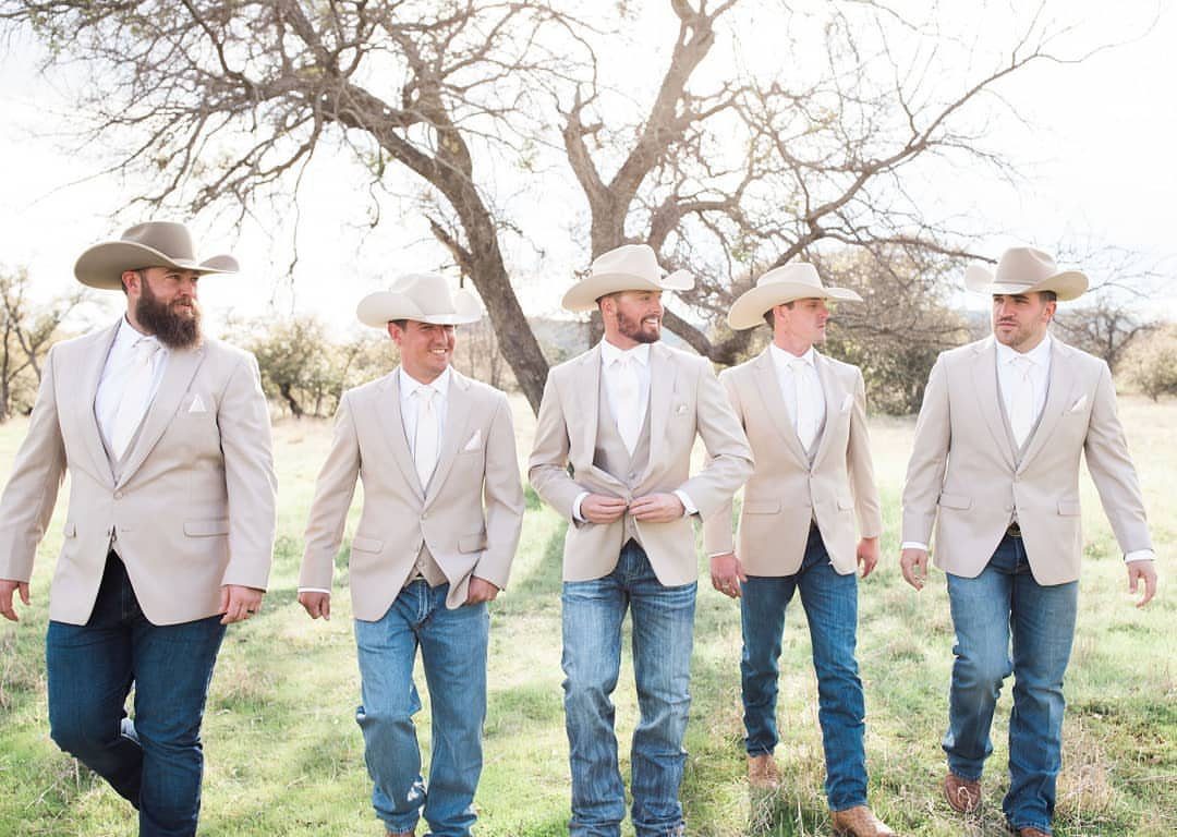 Five men in tan blazers and cowboy hats posing in a rural field.