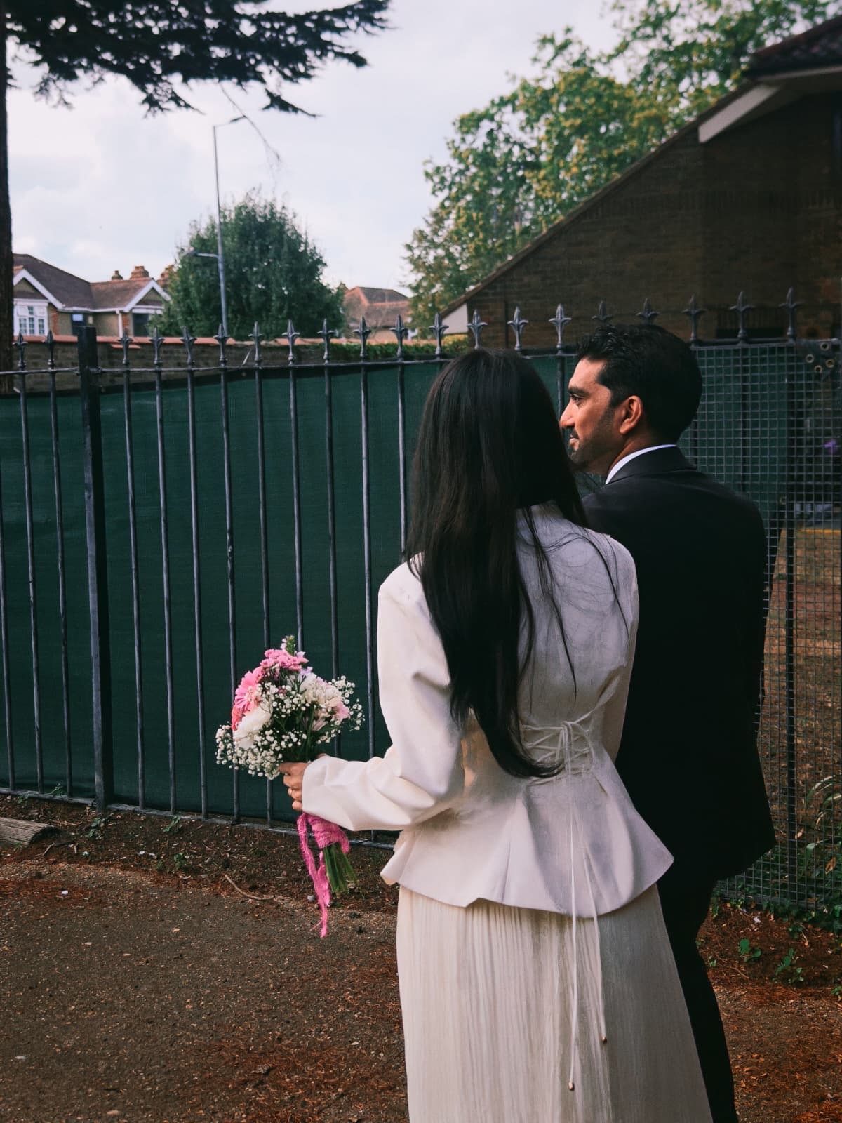 Woman in white blazer and skirt with bouquet and man in black suit.