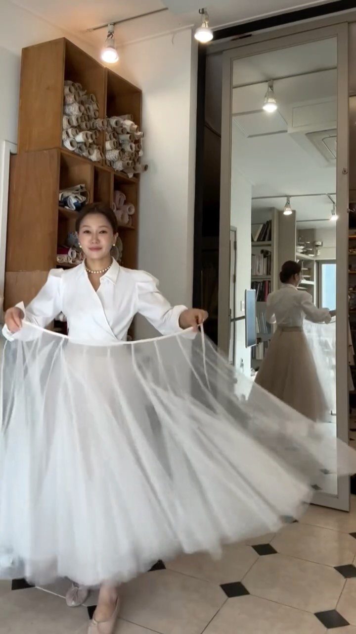 Woman wearing a white blouse and a full white tulle skirt in a studio.
