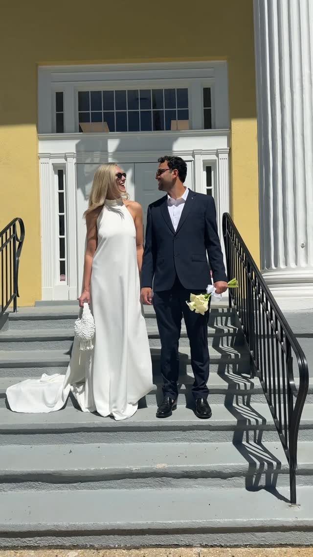 Couple in wedding attire standing on steps in front of a courthouse building.